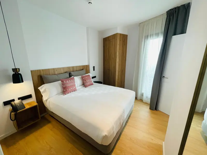 Une chambre lumineuse avec un grand lit et un parquet clair.