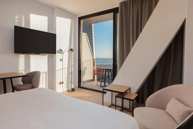 Une chambre lumineuse avec un lit et un espace détente donnant sur un balcon.