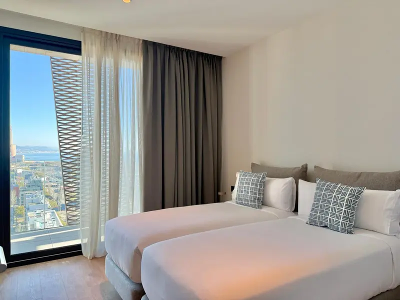 Chambre lumineuse avec deux lits simples et vue sur la mer.