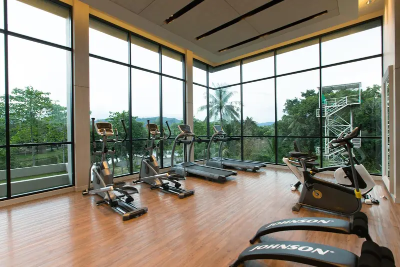 Une salle de sport lumineuse avec des équipements de cardio face à une grande baie vitrée.