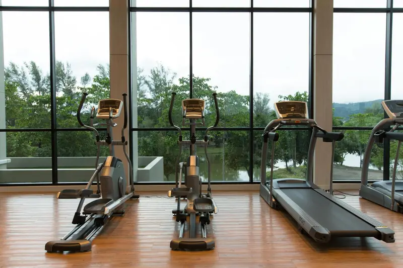 Une salle de sport lumineuse avec des équipements de cardio face à une grande baie vitrée.