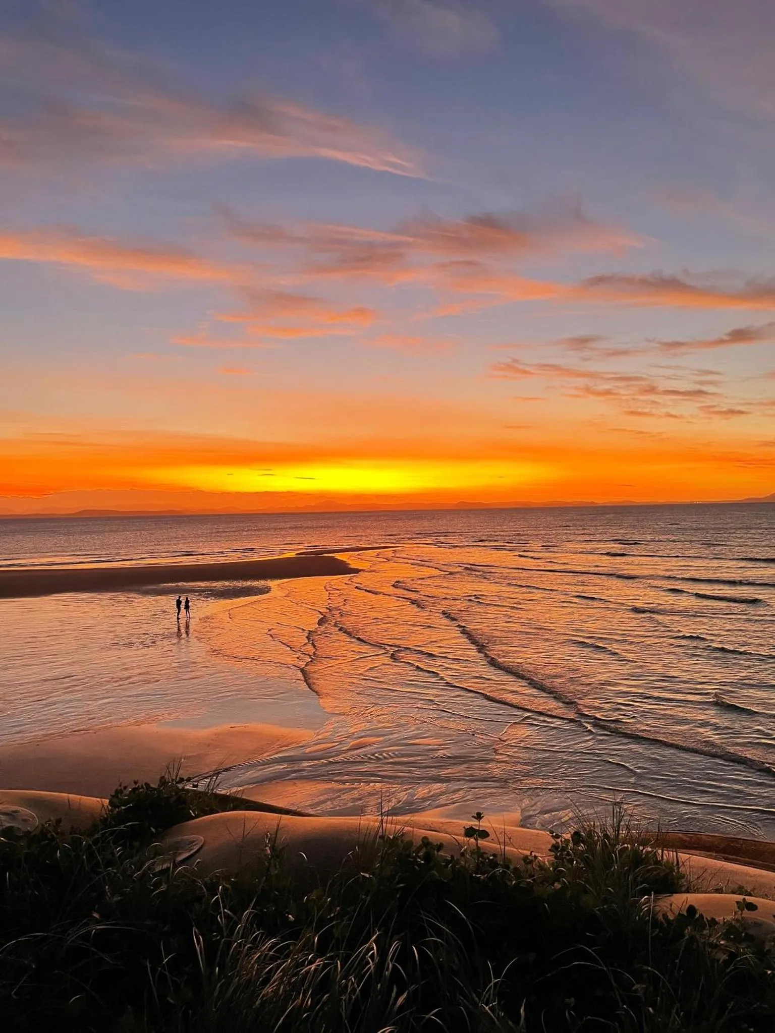 Coucher de soleil sur une plage avec deux personnes marchant dans l'eau.