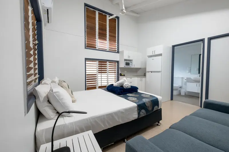 Une chambre lumineuse avec un lit fait et un coin cuisine.