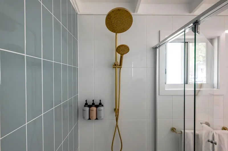Une douche à l'italienne avec des carreaux bleus et une pomme de douche dorée.