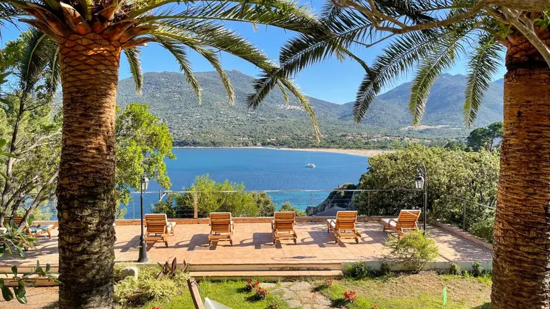 Terrasse ensoleillée avec chaises longues donnant sur une baie et des montagnes.