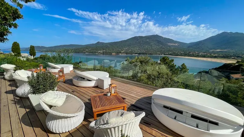 Terrasse aménagée avec mobilier blanc offrant une vue sur la mer et les collines.