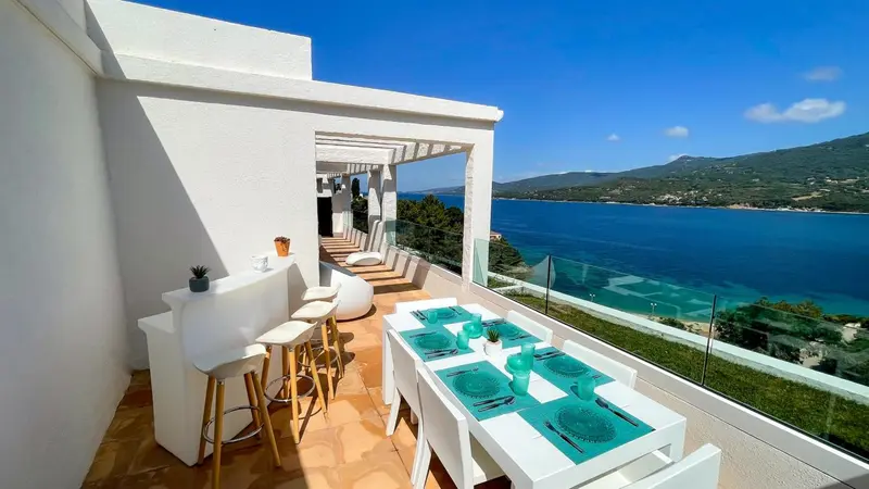 Terrasse aménagée avec table à manger et bar, vue sur la mer et les montagnes.