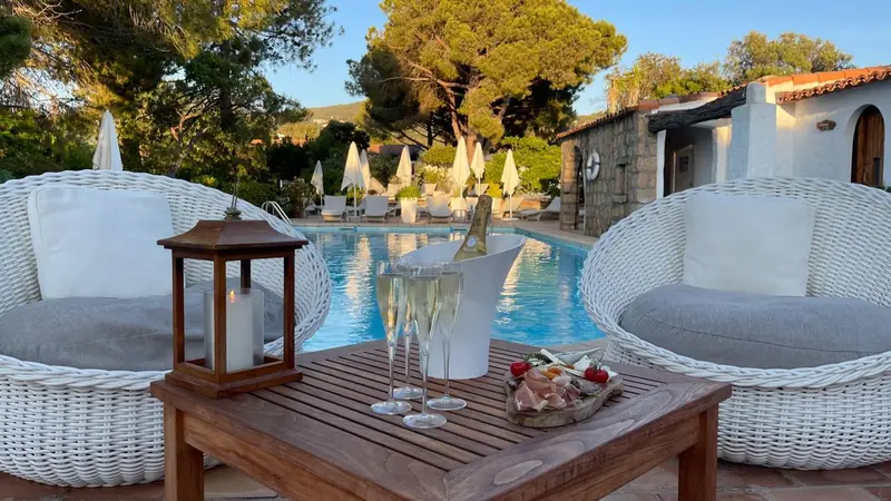 Deux fauteuils en osier entourent une table basse avec des boissons et des amuse-gueules près d'une piscine.