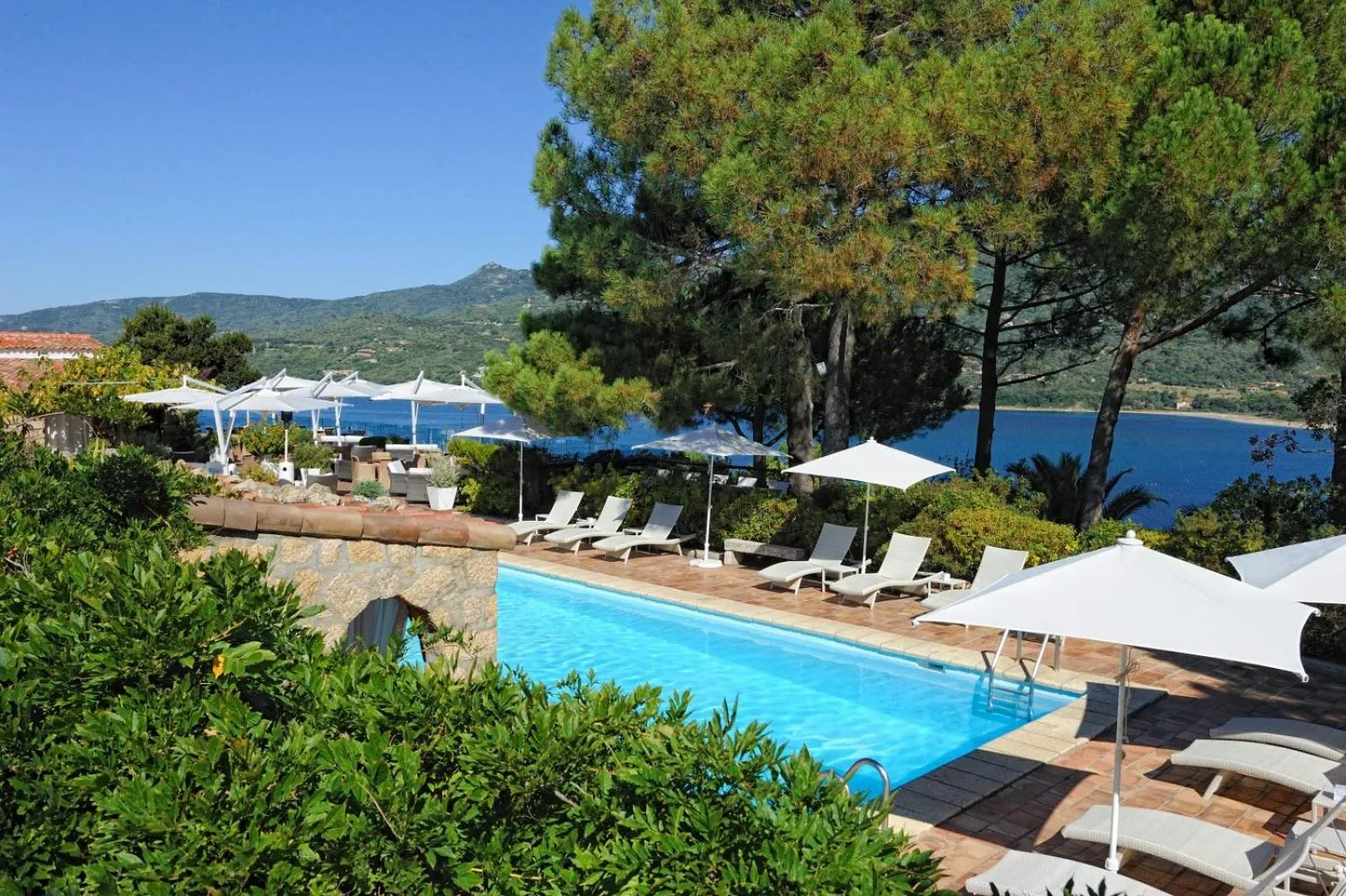 Une piscine bordée de transats blancs sous des parasols, avec une vue sur la mer.