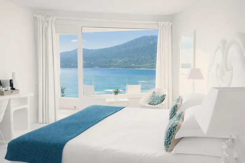 Chambre lumineuse avec un grand lit et vue sur la mer.