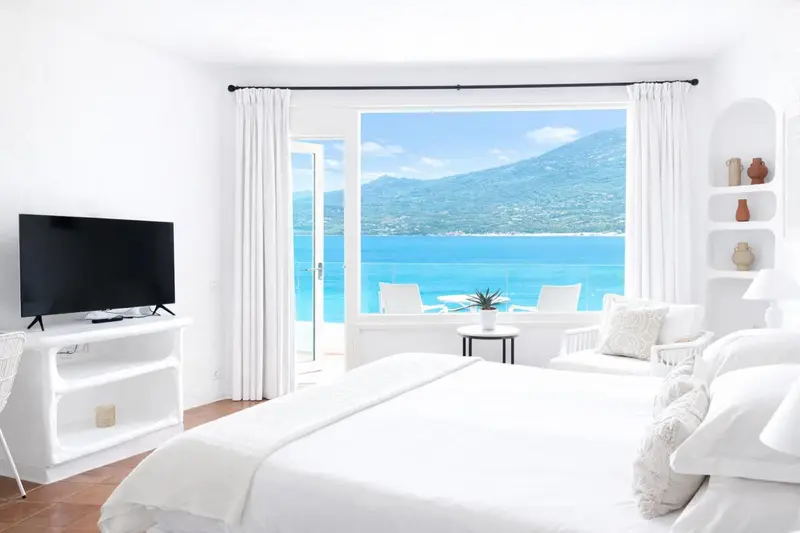 Une chambre lumineuse avec un grand lit blanc et une vue sur la mer.