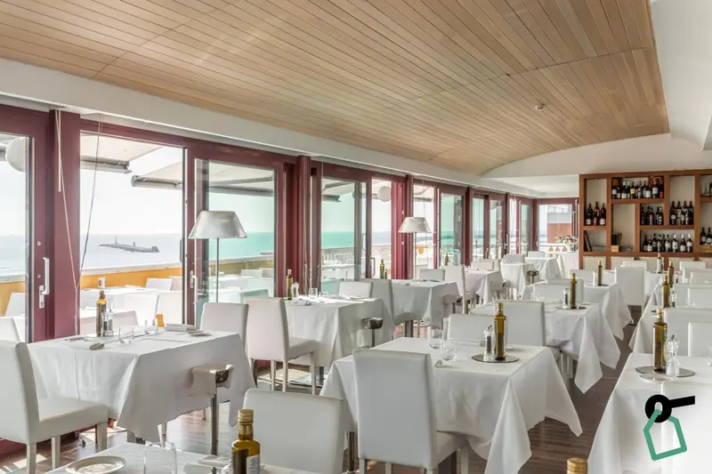 Une salle lumineuse avec des tables dressées face à une vue sur la mer.