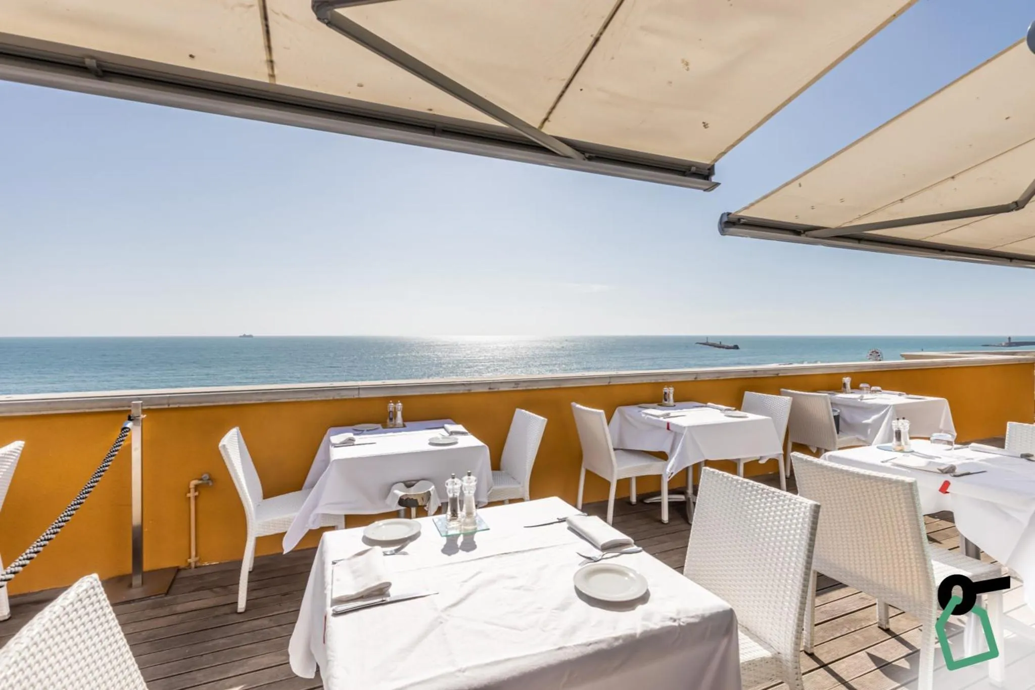 Terrasse avec tables nappées face à la mer.