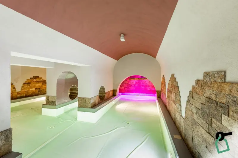 Une piscine intérieure avec un éclairage coloré et des murs en pierre.
