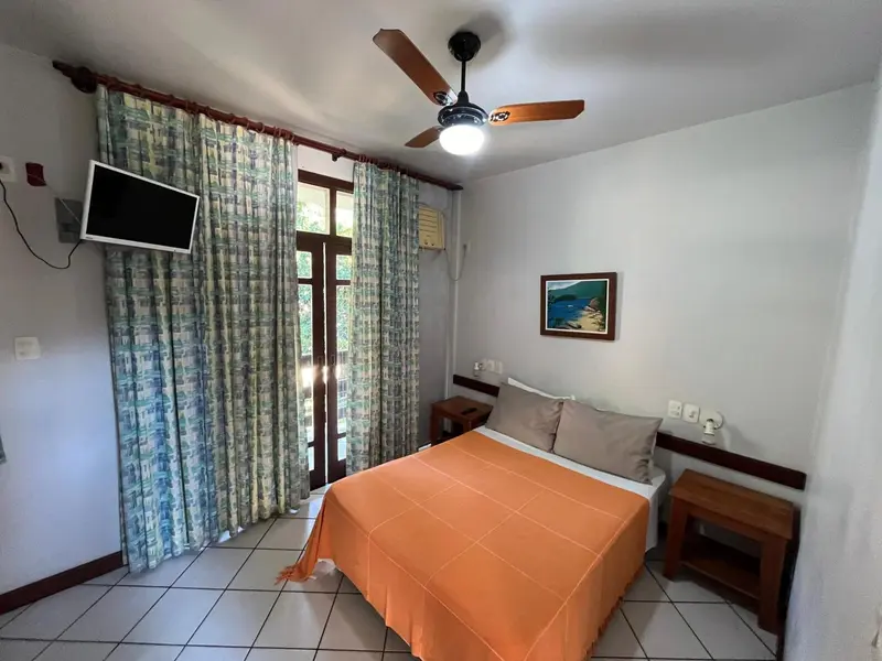 Une chambre lumineuse avec un lit recouvert d'une couverture orange et un téléviseur mural.