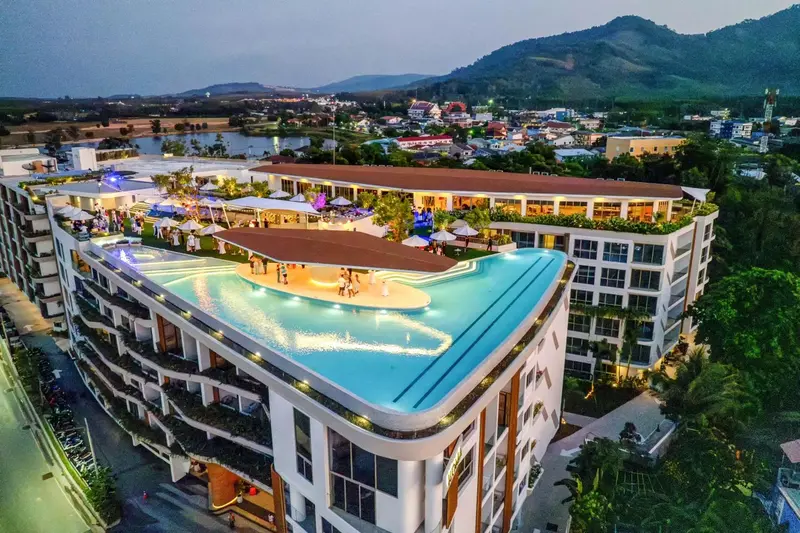 Vue aérienne d'un bâtiment moderne avec une piscine sur le toit et des collines en arrière-plan.
