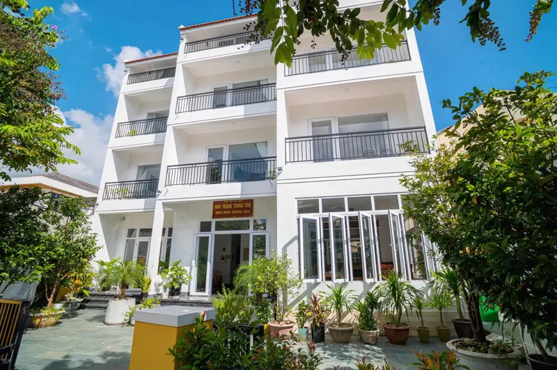 Façade d'un bâtiment blanc à plusieurs étages avec des balcons et une végétation luxuriante.
