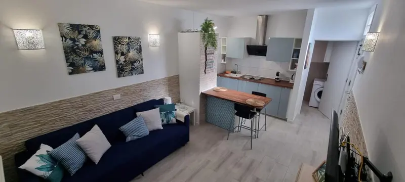 Un espace de vie lumineux combine un coin salon avec un canapé bleu foncé et une cuisine équipée.