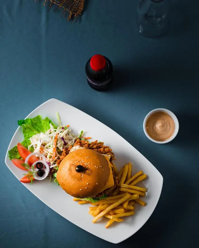 Assiette rectangulaire blanche garnie d'un hamburger, de frites et d'une sauce.