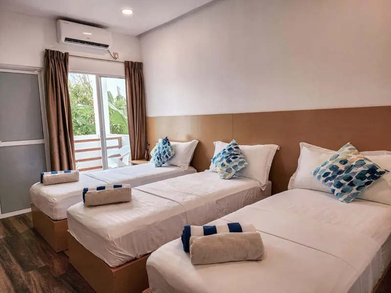Chambre lumineuse avec trois lits simples et une vue sur la végétation.