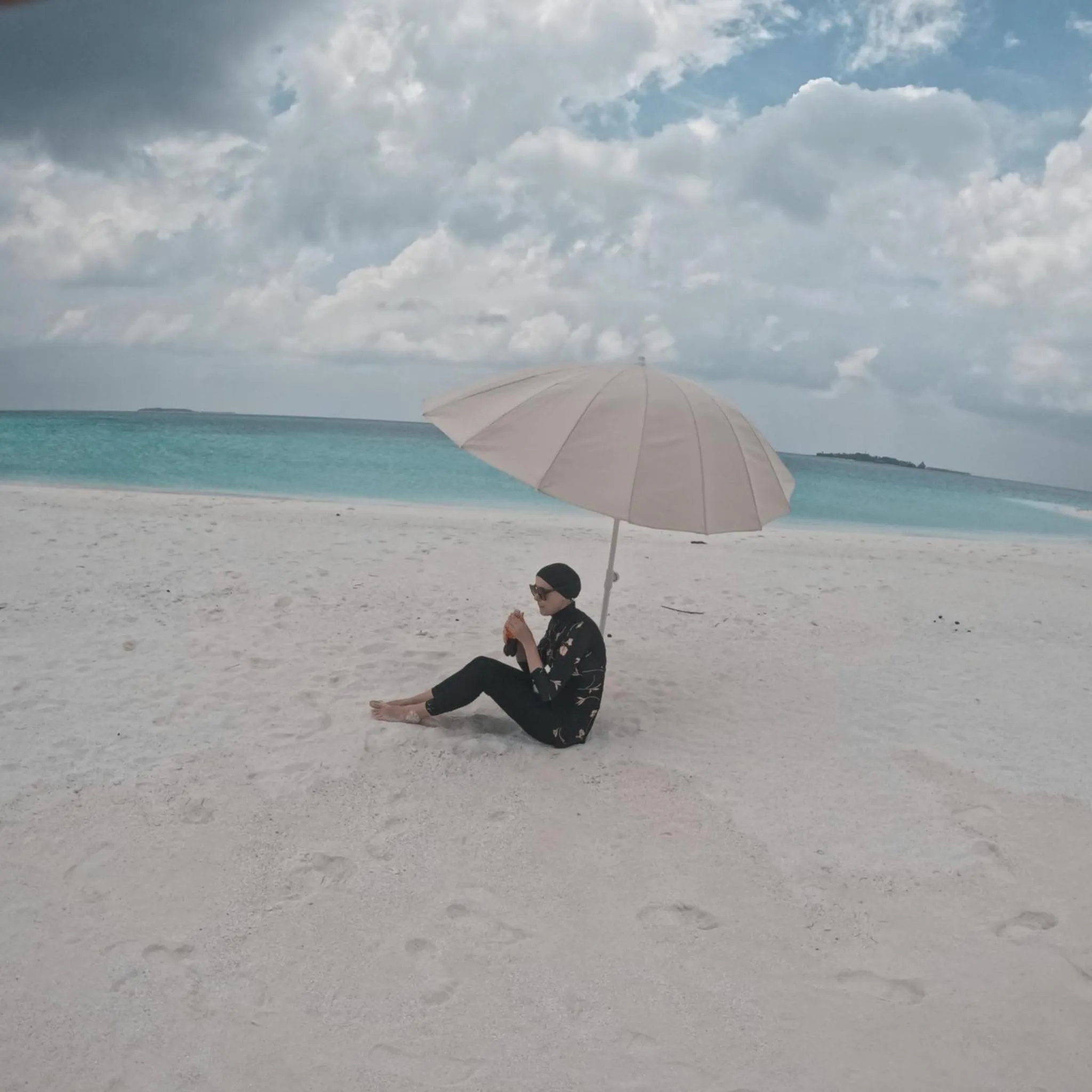 Une personne assise sur une plage de sable blanc, à l'ombre d'un parasol.