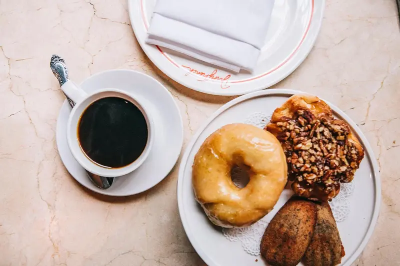 Une tasse de café, un beignet et une viennoiserie sont présentés sur une table.