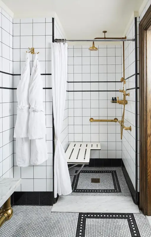 Une douche à l'italienne carrelée de noir et blanc avec un rideau blanc.