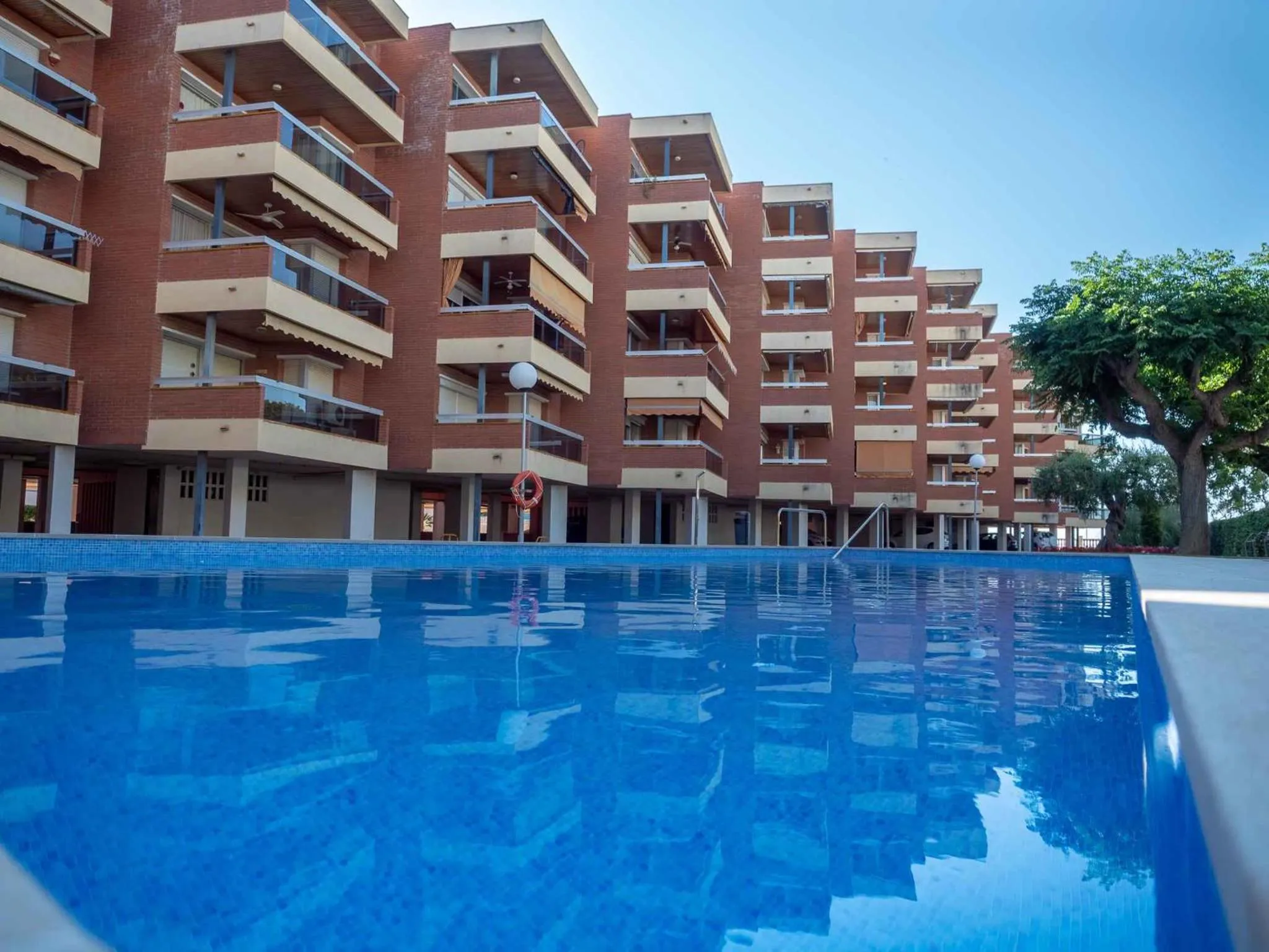 Bâtiment à plusieurs étages avec des balcons donnant sur une piscine bleu clair.