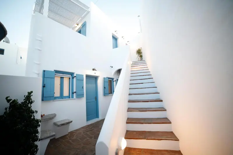 Escalier blanc montant vers des fenêtres bleues dans une cour intérieure.