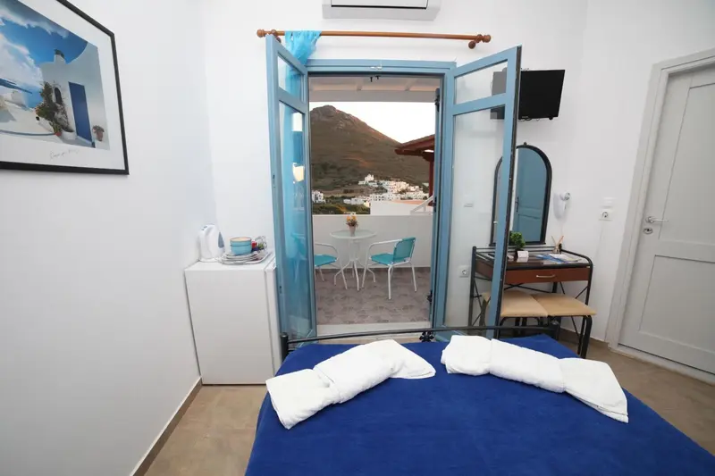 Une chambre lumineuse s'ouvre sur une terrasse avec vue sur un village.