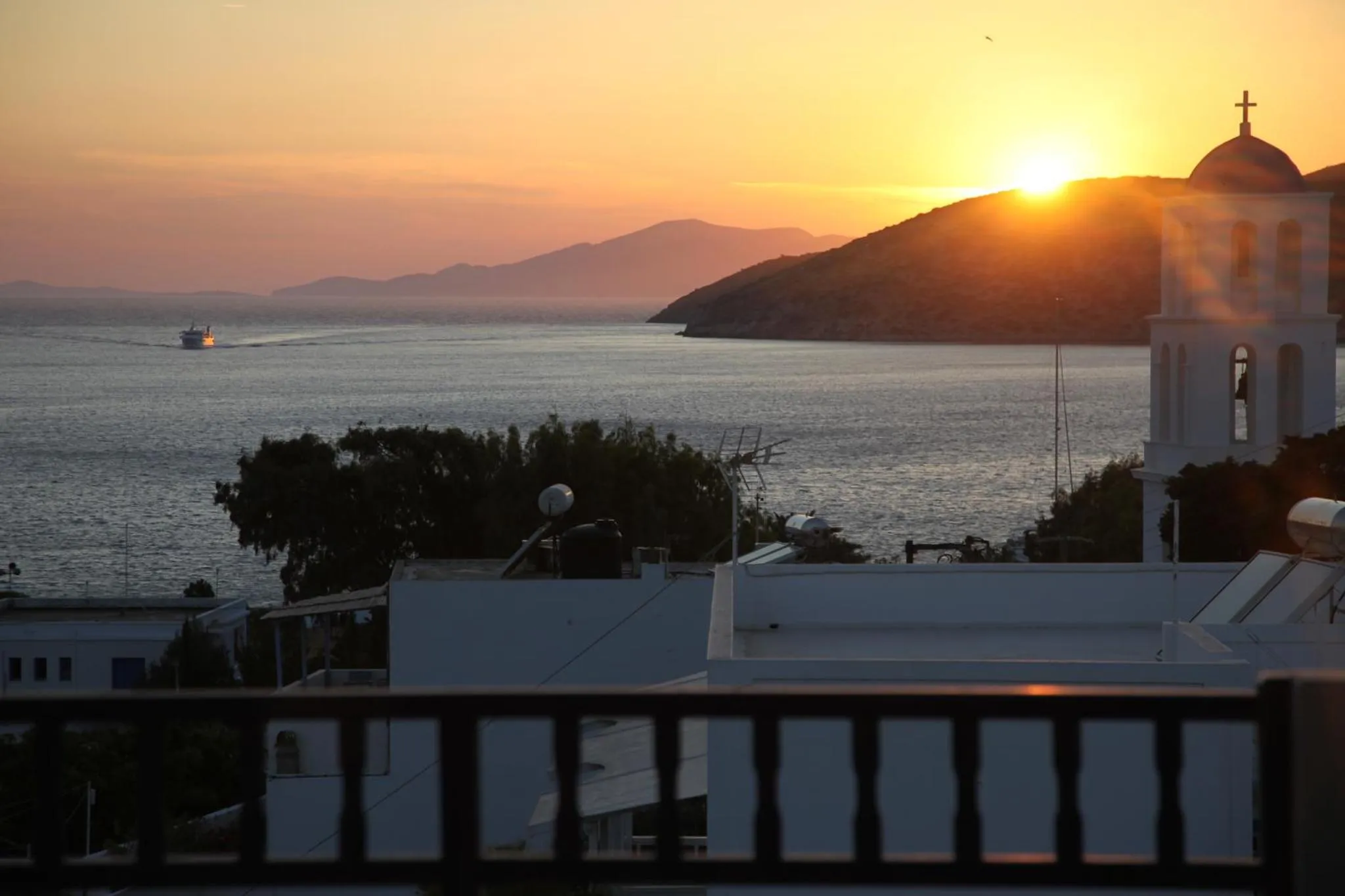 Vue sur la mer au coucher du soleil avec un bâtiment religieux et une colline en arrière-plan.