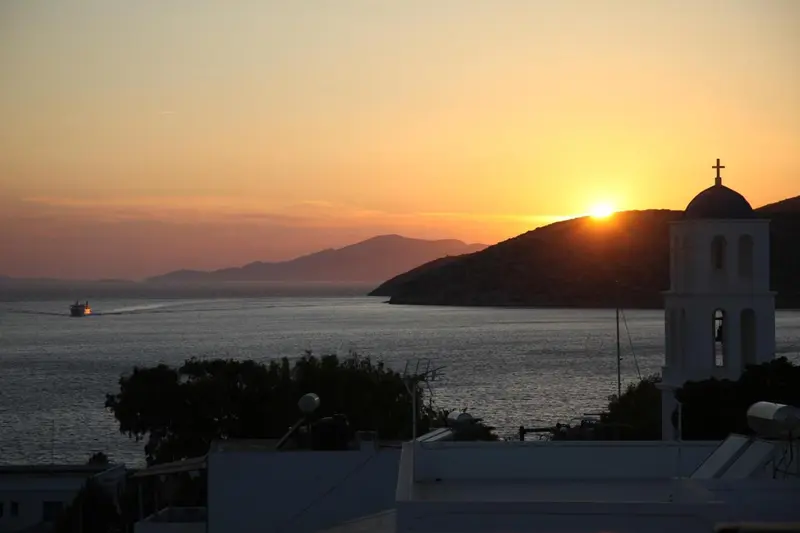 Coucher de soleil sur la mer avec un bâtiment blanc et une colline en arrière-plan.