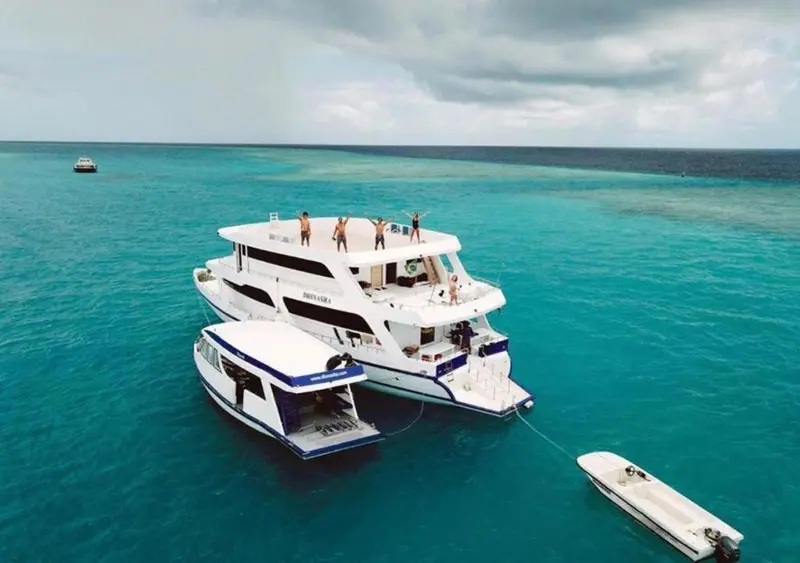Un bateau blanc à deux coques navigue sur une mer turquoise sous un ciel nuageux.