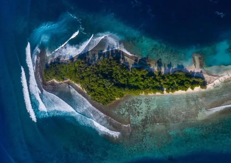 Vue aérienne d'une île tropicale entourée d'eaux turquoise et de vagues.