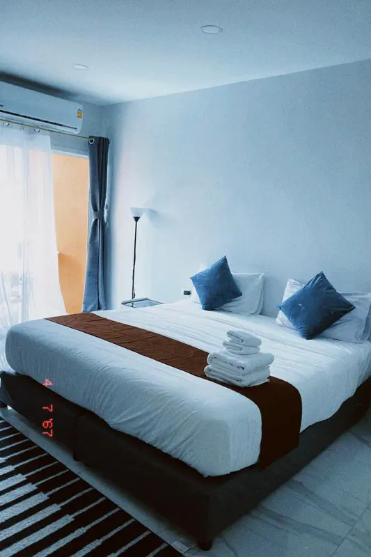 Une chambre lumineuse avec un grand lit recouvert d'une courtepointe blanche et de coussins bleus.