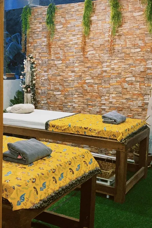 Deux tables de massage sont prêtes dans une salle décorée de plantes et de murs en pierre.
