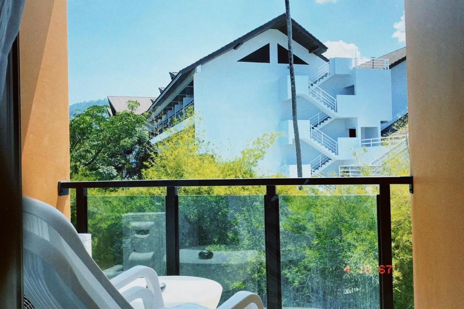 Vue sur des bâtiments blancs et une végétation luxuriante depuis un balcon.