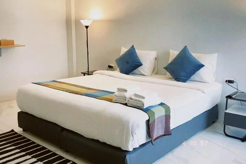 Une chambre lumineuse avec un grand lit recouvert d'une courtepointe colorée et de coussins bleus.