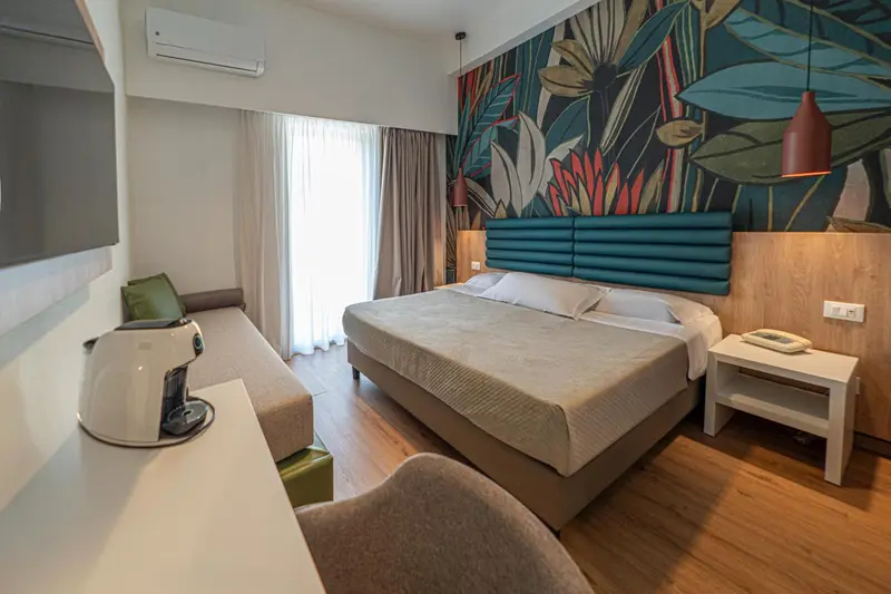 Une chambre lumineuse avec un grand lit et un mur décoré de motifs tropicaux.