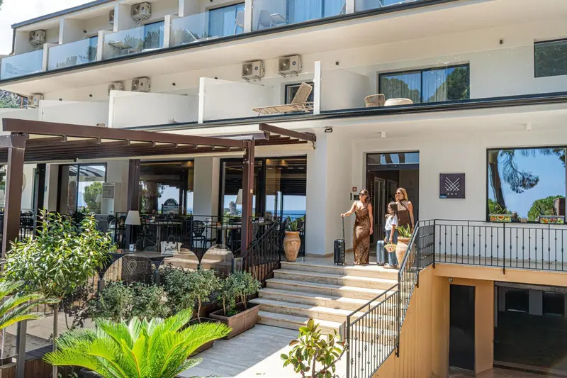 Façade d'un bâtiment blanc avec une entrée et des terrasses ensoleillées.