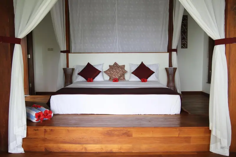 Un lit king-size avec une moustiquaire blanche dans une chambre décorée de bois sombre.
