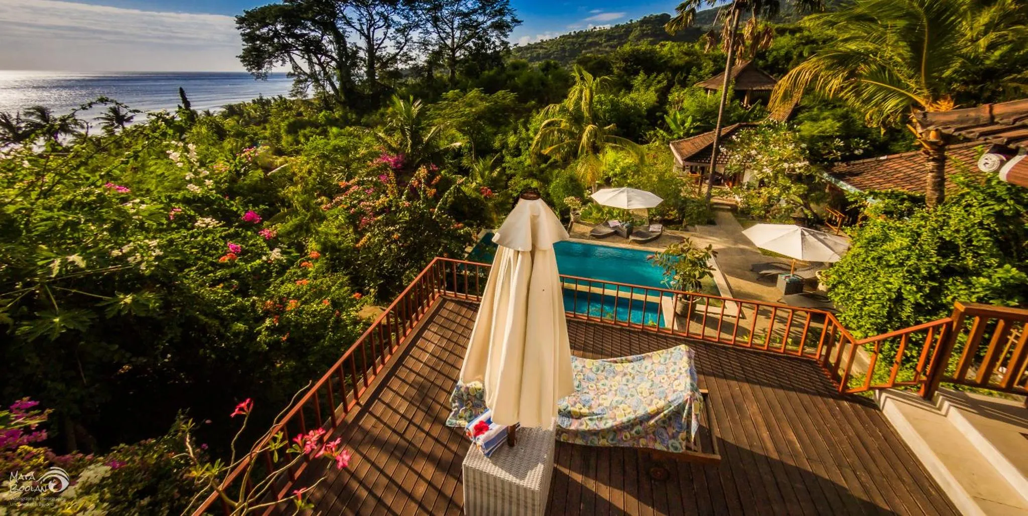 Terrasse en bois avec transats et vue sur une piscine et la végétation.