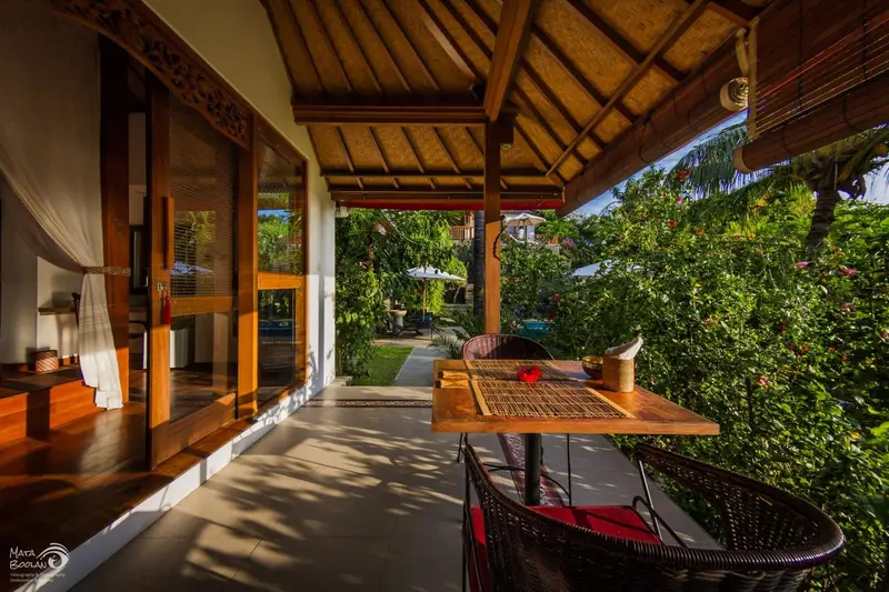 Terrasse ombragée avec table et chaises en bois donnant sur une végétation luxuriante.