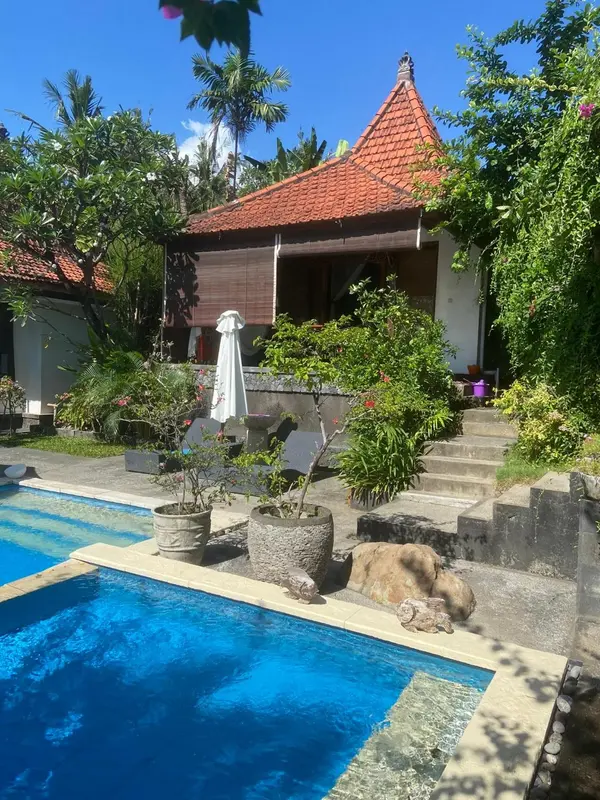 Bâtiment à toit rouge et piscine entourée de végétation tropicale.
