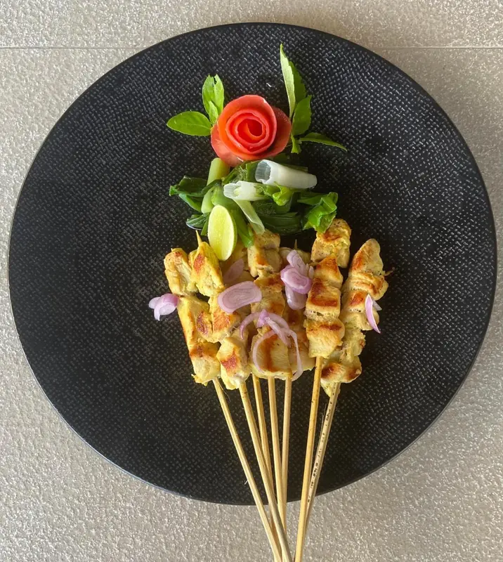 Présentation soignée de brochettes de poulet marinées, accompagnées de légumes frais et d'une décoration florale.
