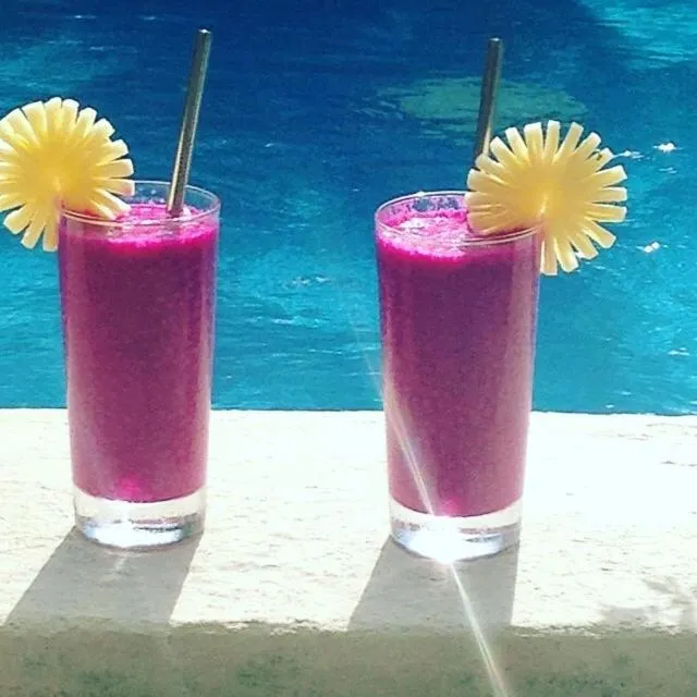 Deux verres de boisson rose décorés de tranches d'ananas reposent sur une surface claire au bord d'une piscine.