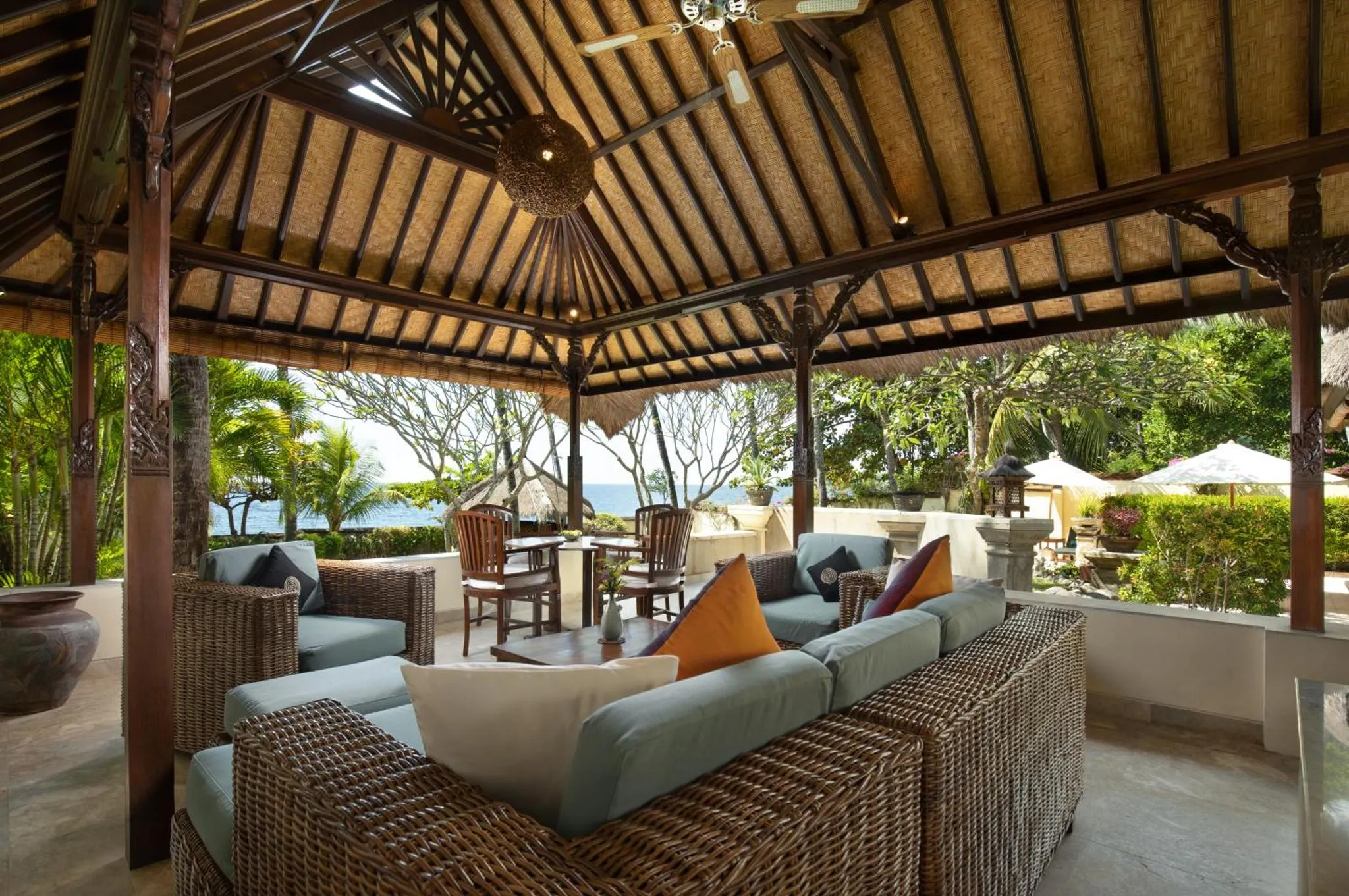 Espace de détente extérieur avec mobilier en rotin et vue sur la mer.