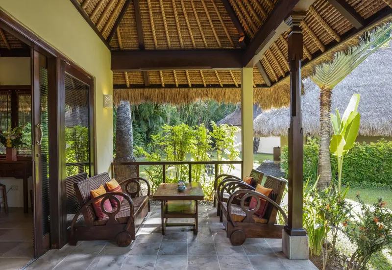Terrasse ombragée avec mobilier en bois et végétation luxuriante.