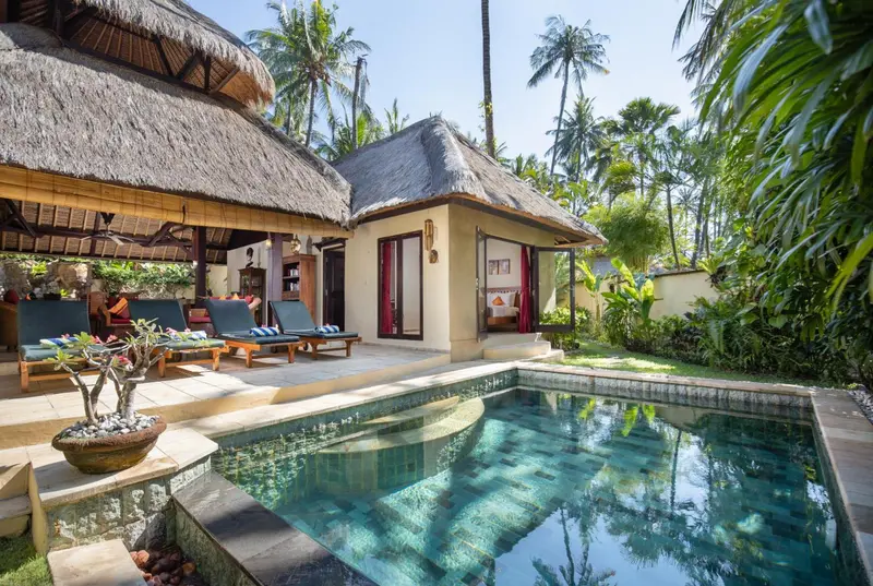 Petites villas avec toits de chaume s'ouvrent sur une piscine et une terrasse.