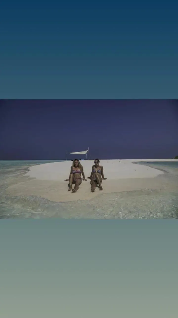 Deux personnes se détendent sur une plage de sable blanc face à une mer turquoise.